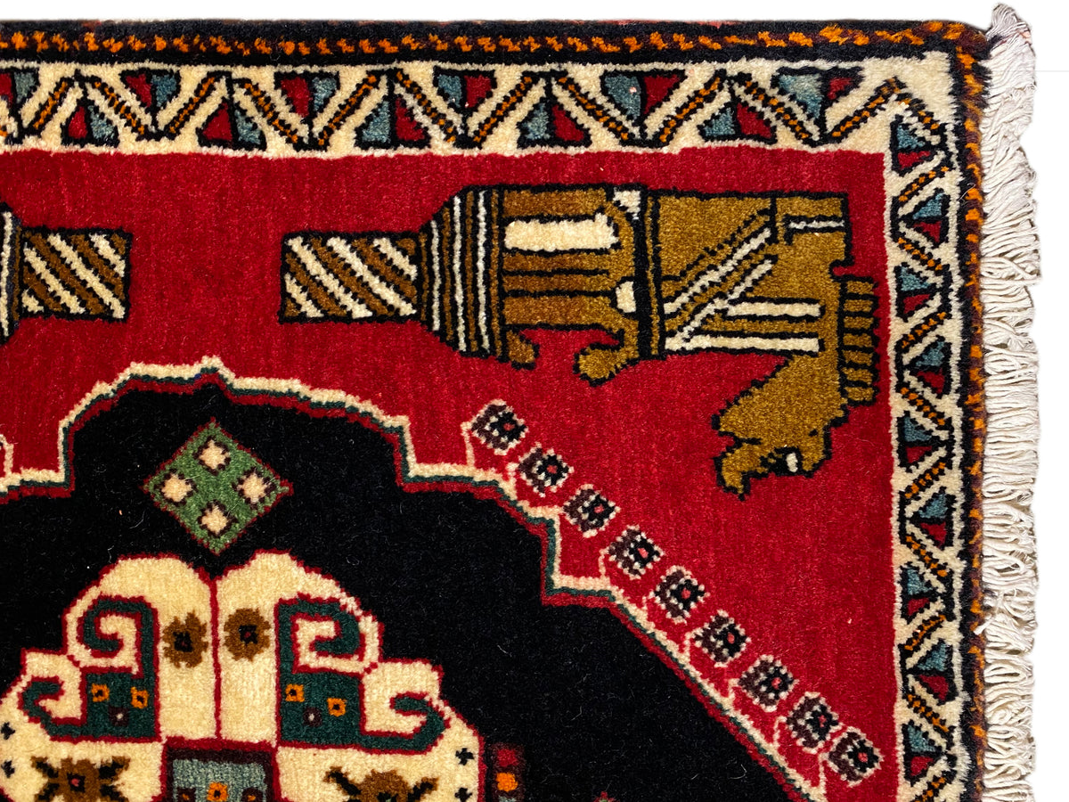 Alfombra Poshti de 63x55 cm: detalle del borde con flecos y una franja ornamental multicolor sobre fondo rojo