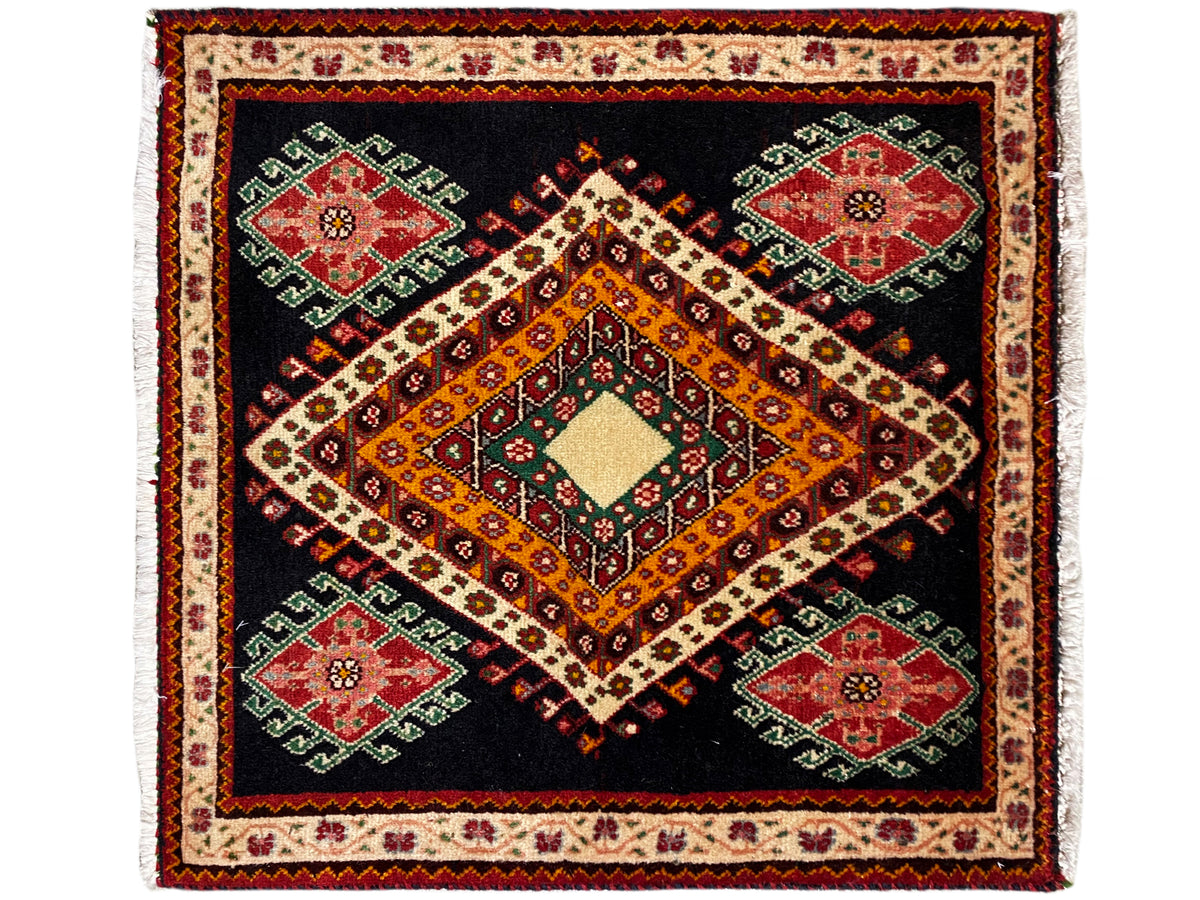 Alfombra Poshti con fondo negro, rombo naranja-amarillo y cuatro medallones verdes y rojos