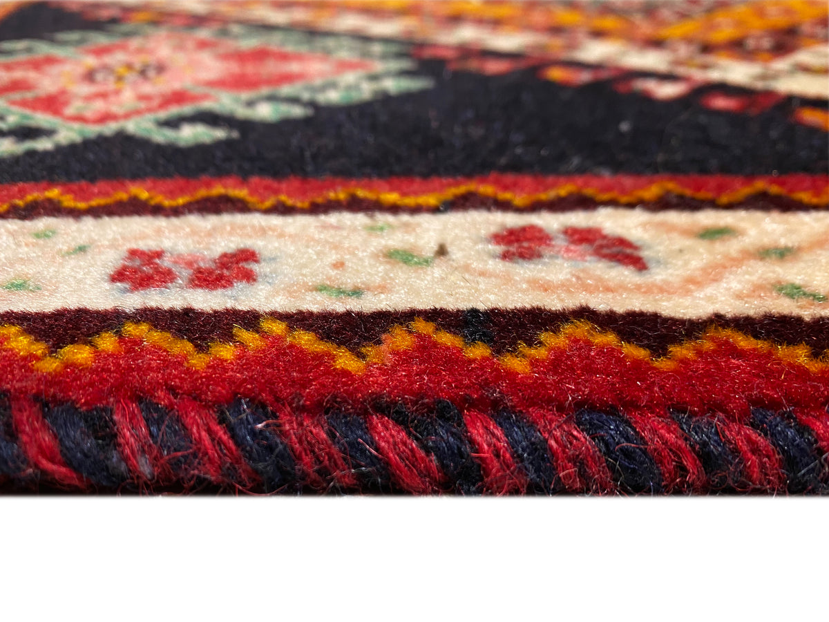 Detalle del borde de la alfombra Poshti: cenefa multicolor y flecos oscuros
