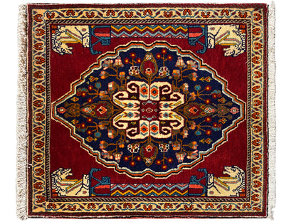 Alfombra rectangular con fondo rojo, motivos ornamentales azul oscuro y ribetes decorativos beige