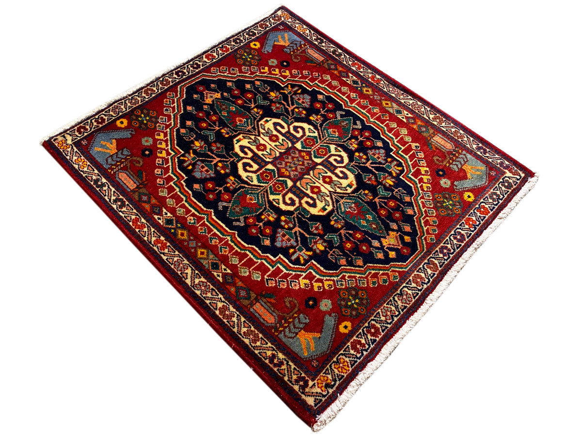 Alfombra cuadrada de 67x60 cm, con fondo rojo y ornamentación central en azul oscuro y dorado