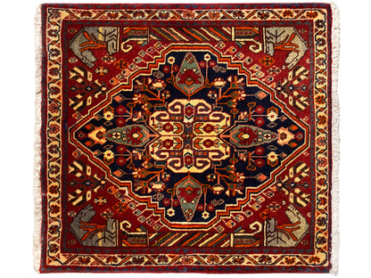 Alfombra de 65x59 cm con fondo rojo, ornamentos azul grisáceos y patrón simétrico