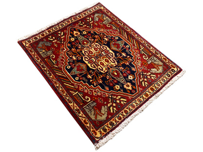 Alfombra de 65x59 cm en vista girada: borde rojo, dibujos oscuros, flecos laterales