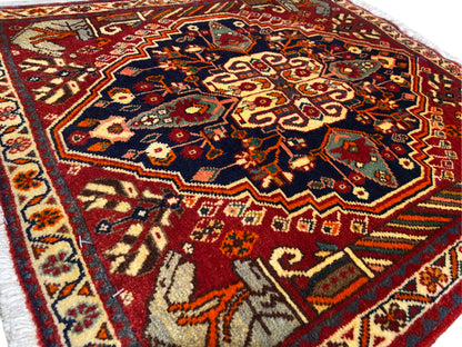 Alfombra de 65x59 cm en primer plano: campo ornamental central en tonos azules, rojos y dorados