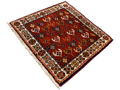 Alfombra de 61x61 cm con un campo de estampado rojo, cenefa multicolor y bordes deshilachados