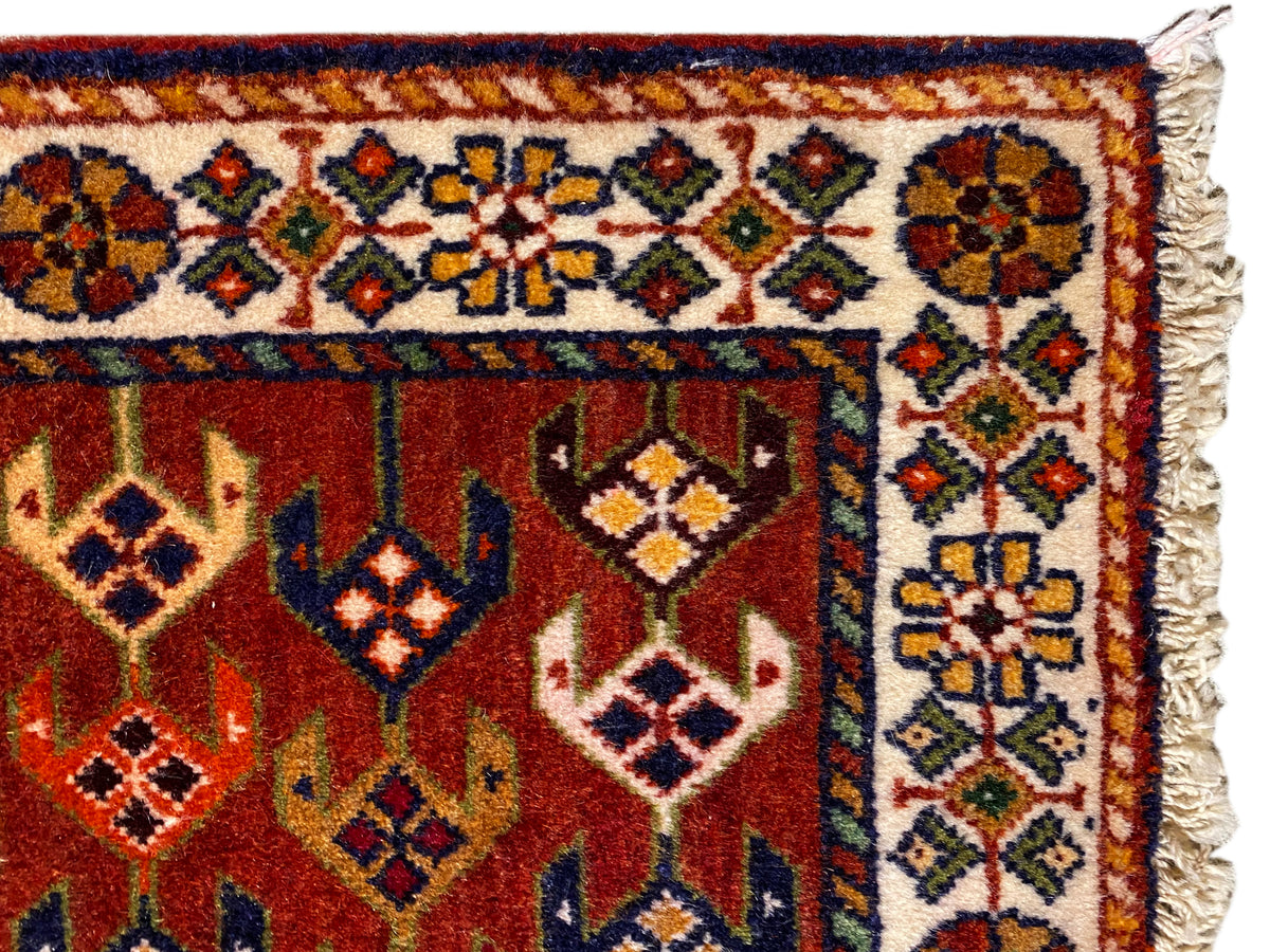 Detalle de alfombra: superficie roja con cenefa ornamental, rombos de colores y bordes laterales deshilachados