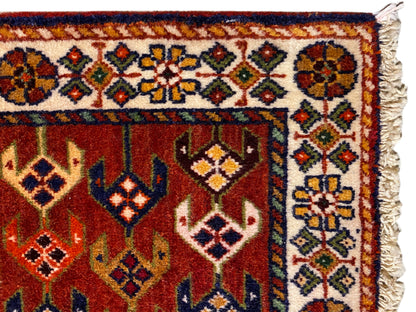 Detalle de alfombra: superficie roja con cenefa ornamental, rombos de colores y bordes laterales deshilachados