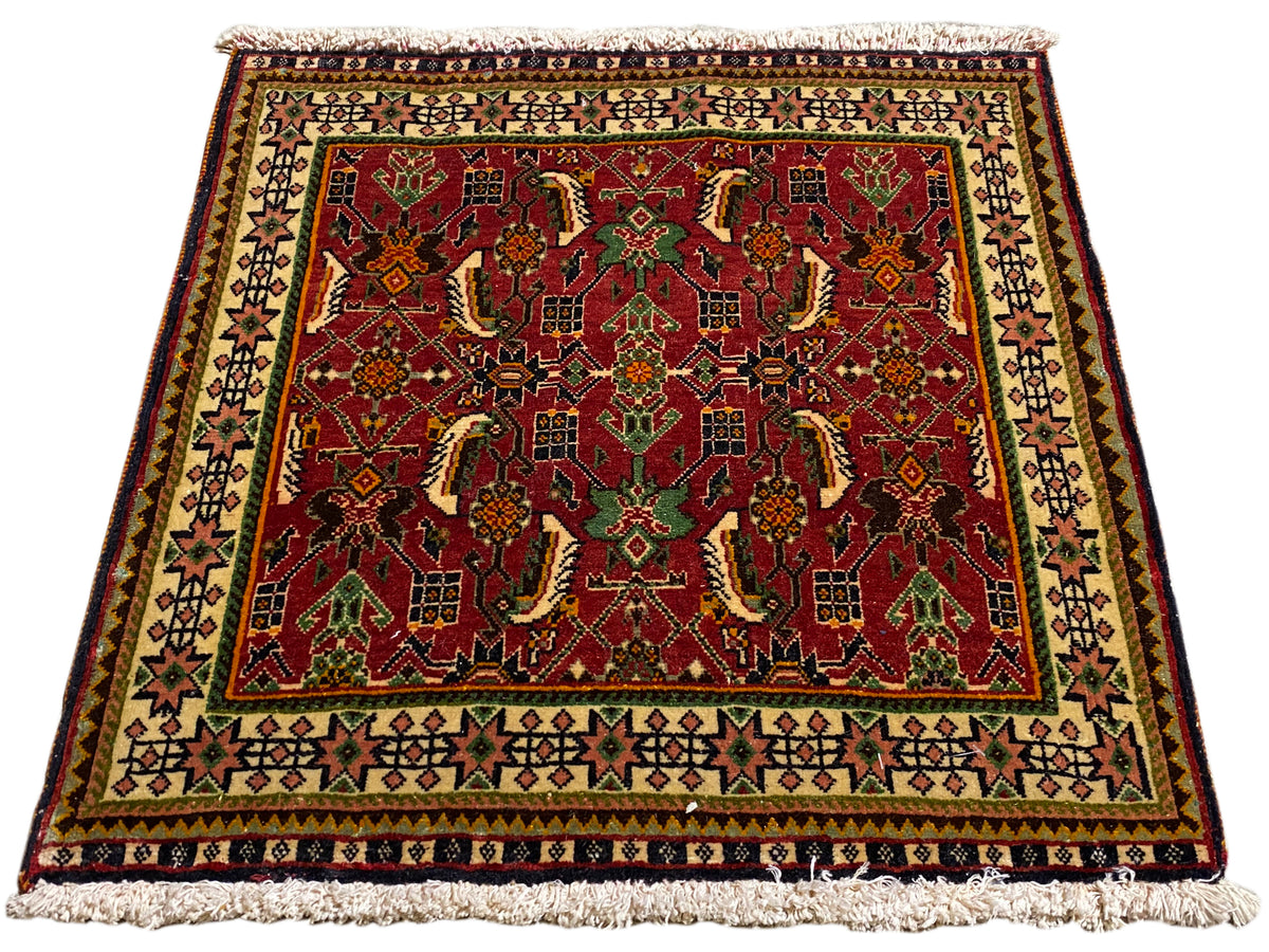 Alfombra Poshti de 63x61 cm, vista en diagonal: motivo ornamental rojo en verde y beige.