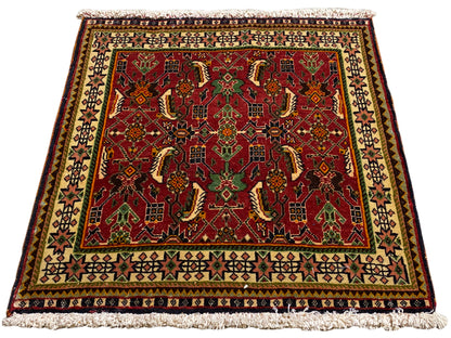 Alfombra Poshti de 63x61 cm, vista en diagonal: motivo ornamental rojo en verde y beige.