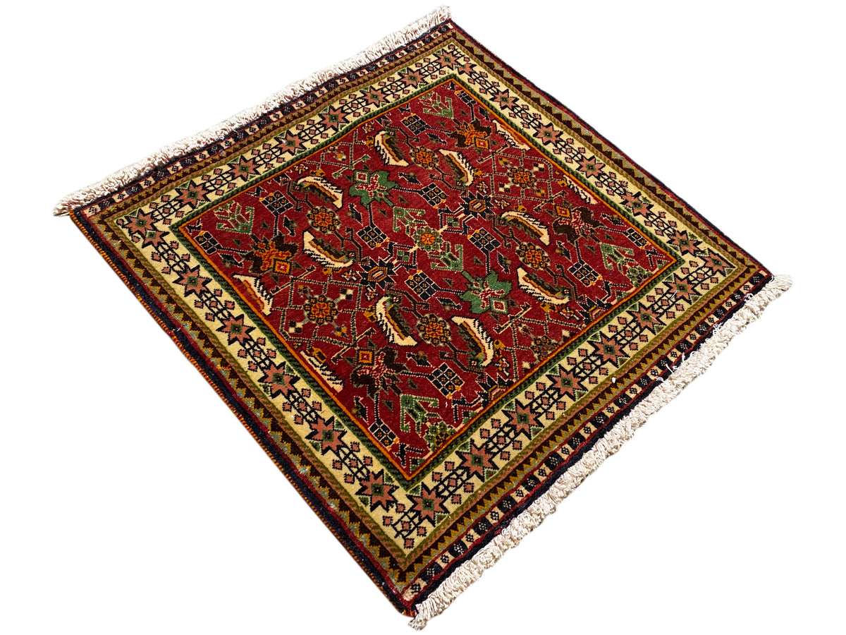 Alfombra Poshti de 63x61 cm, vista diagonal: patrón rojo con detalles verdes, flecos.