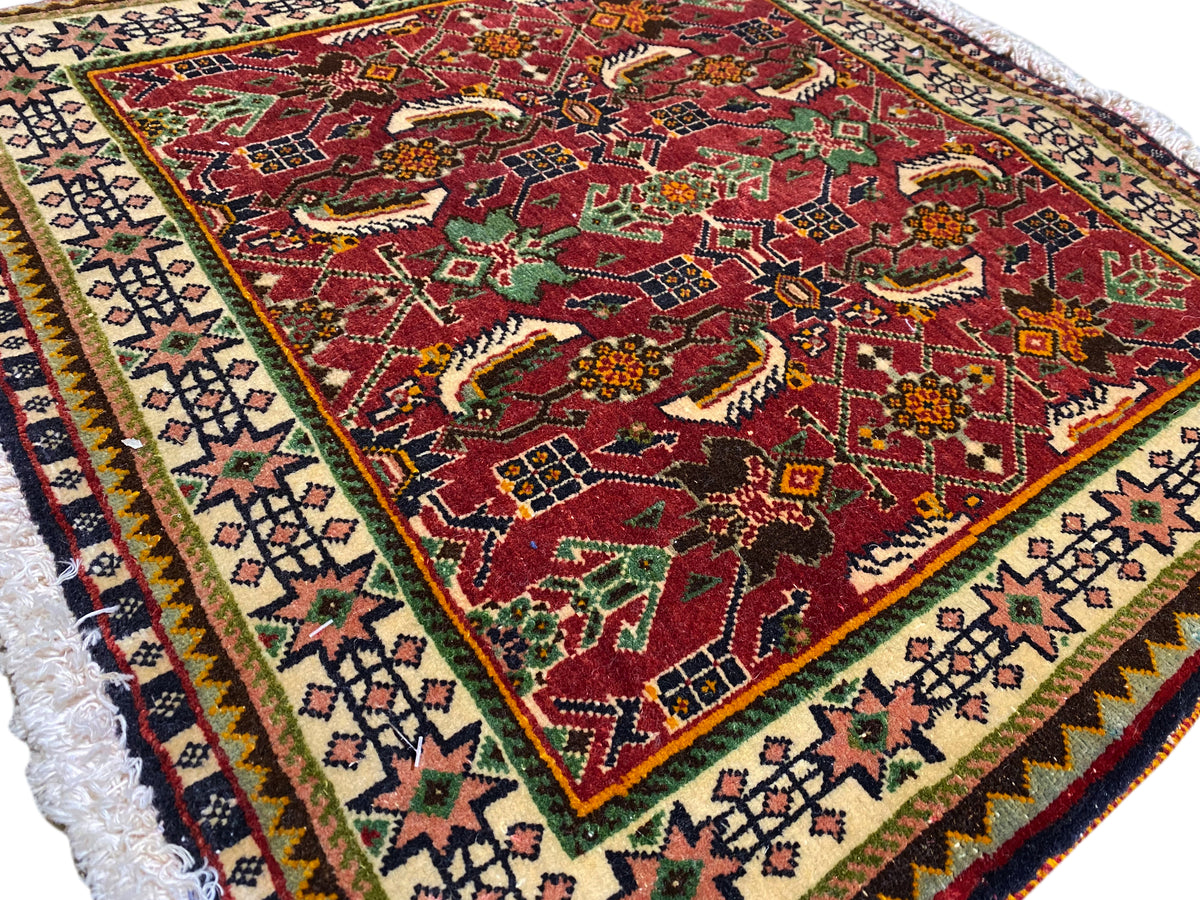 Alfombra Poshti de 63x61 cm, vista detallada: patrón rojo con motivos de animales y ornamentos, y cenefa.
