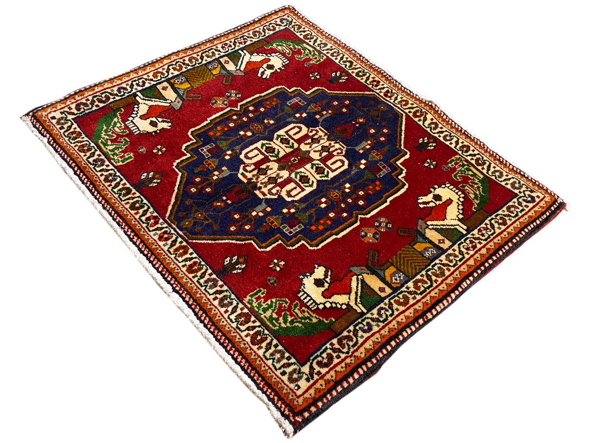 Alfombra Posh­ti con forma de rombos, fondo rojo, medallón azul y motivos de animales