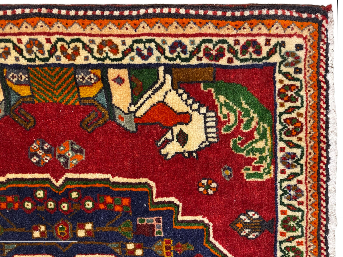 Primer plano de una alfombra Poshti, campo rojo con animales, borde decorativo azul y cenefa estampada
