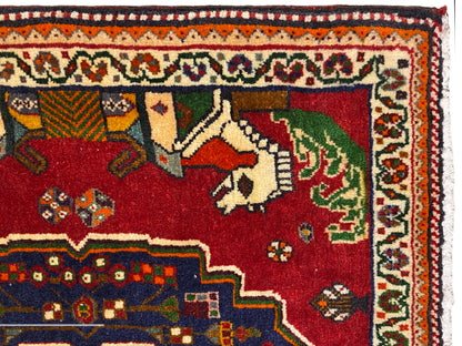 Primer plano de una alfombra Poshti, campo rojo con animales, borde decorativo azul y cenefa estampada