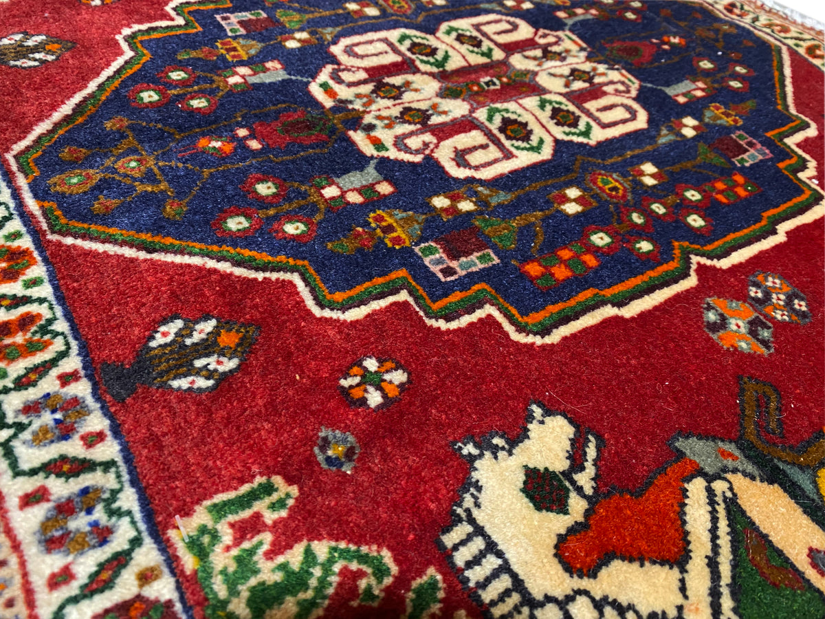 Primer plano de una alfombra Poshti, campo rojo con una corona ornamental azul y motivos de animales