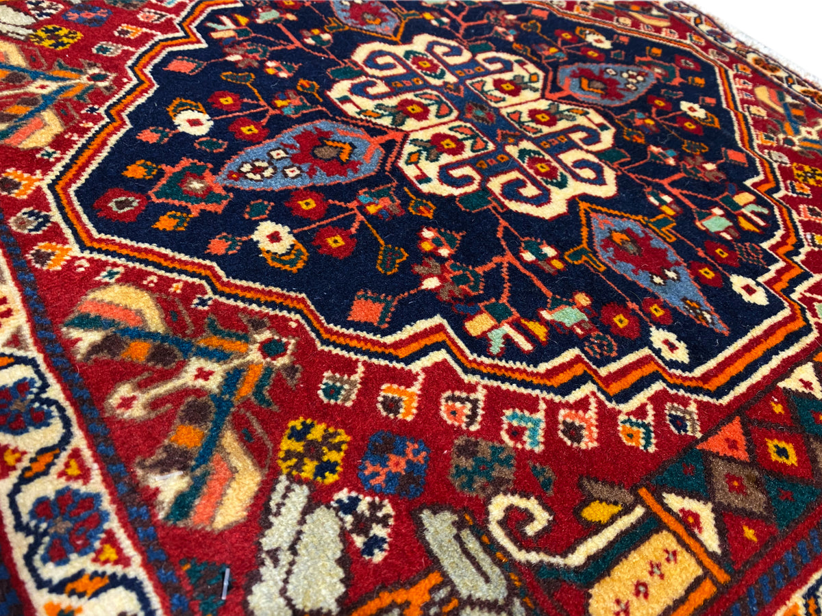 Primer plano de una alfombra: patrón azul con ornamentos rojos y amarillos, textura tejida