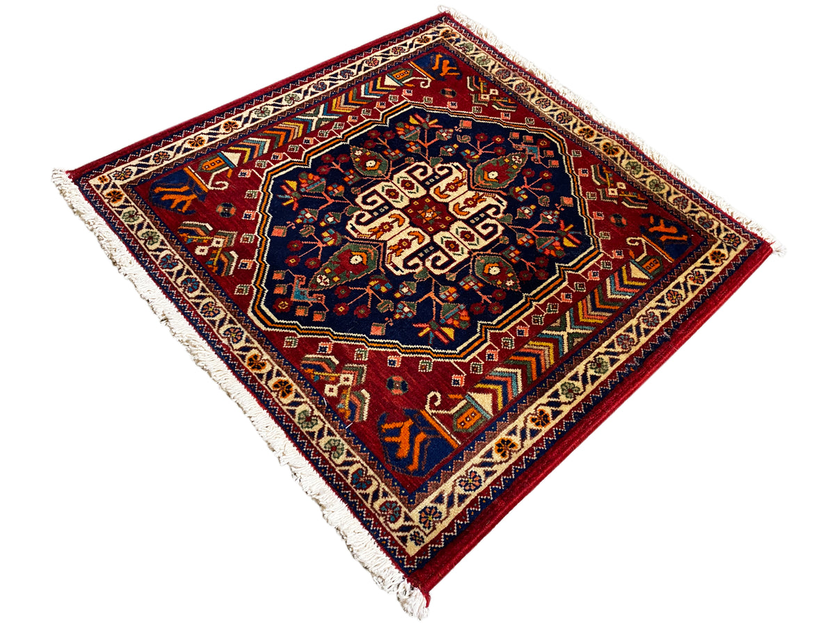 Alfombra de 63x60 cm con vista diagonal: centro azul oscuro, borde rojo, flecos