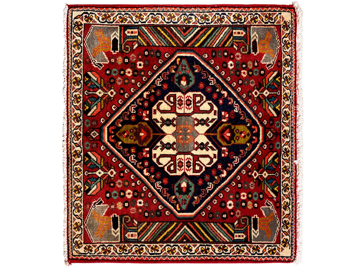 Alfombra oriental con fondo rojo, medallón azul oscuro y ornamentos geométricos