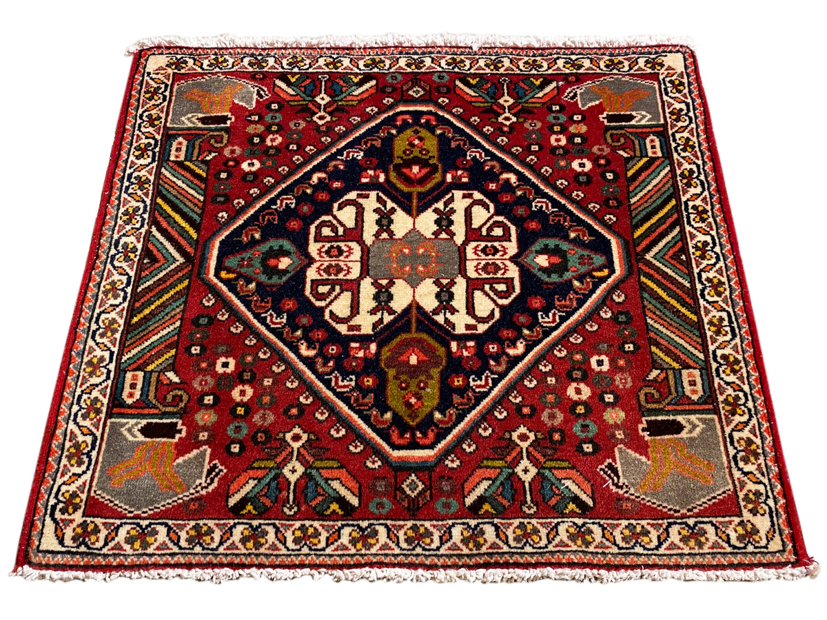 Alfombra oriental rectangular con diseño rojo, marco interior azul y ornamentos en los bordes