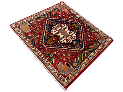 Alfombra oriental con fondo rojo, formas de color crema y franjas decorativas de colores