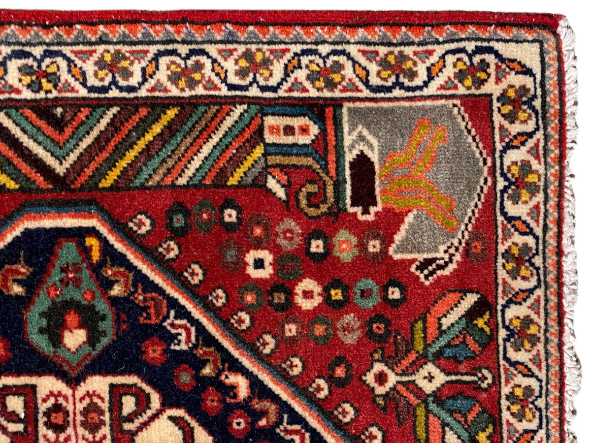 Vista detallada: alfombra roja con motivos ornamentales, cenefa multicolor y flecos