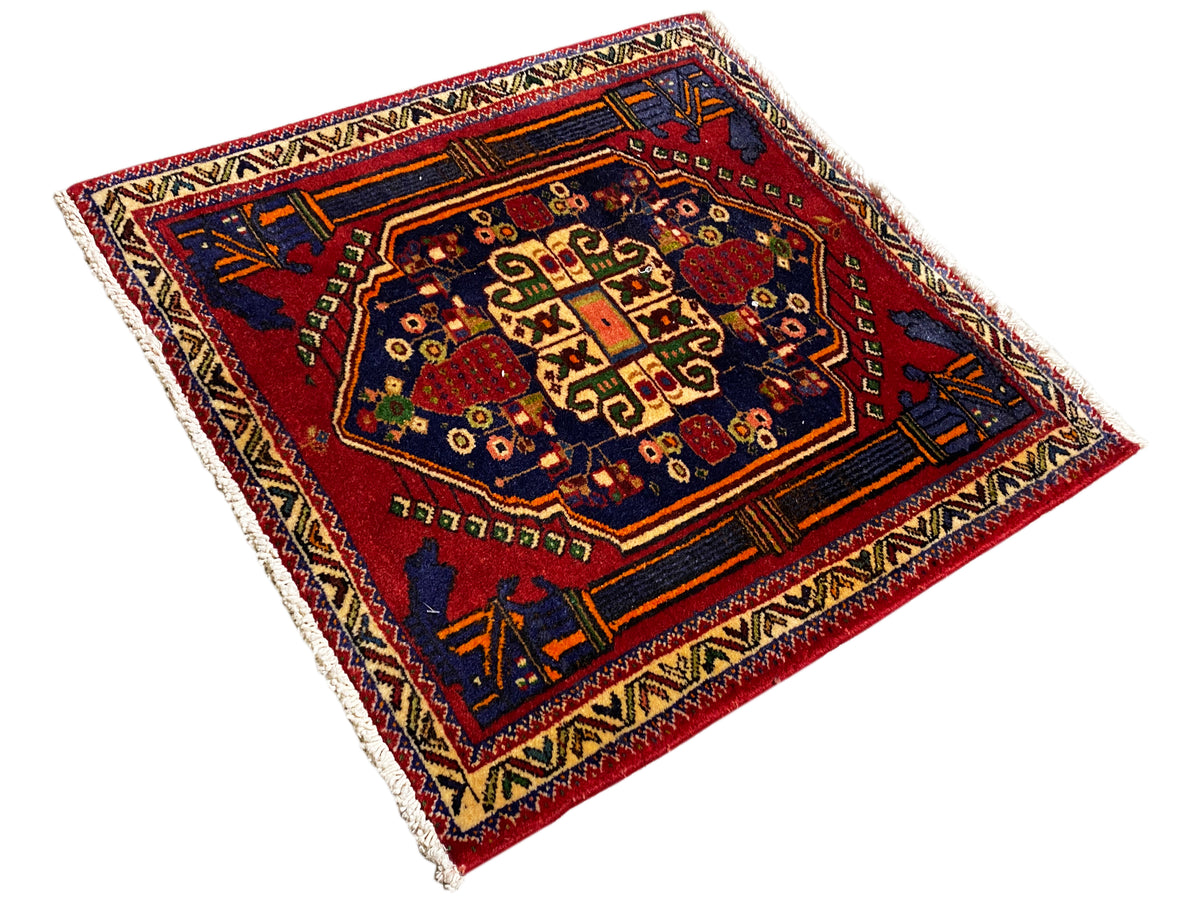 Alfombra Poshti de 66x62 cm en diagonal: cenefa azul y roja con numerosos ornamentos.