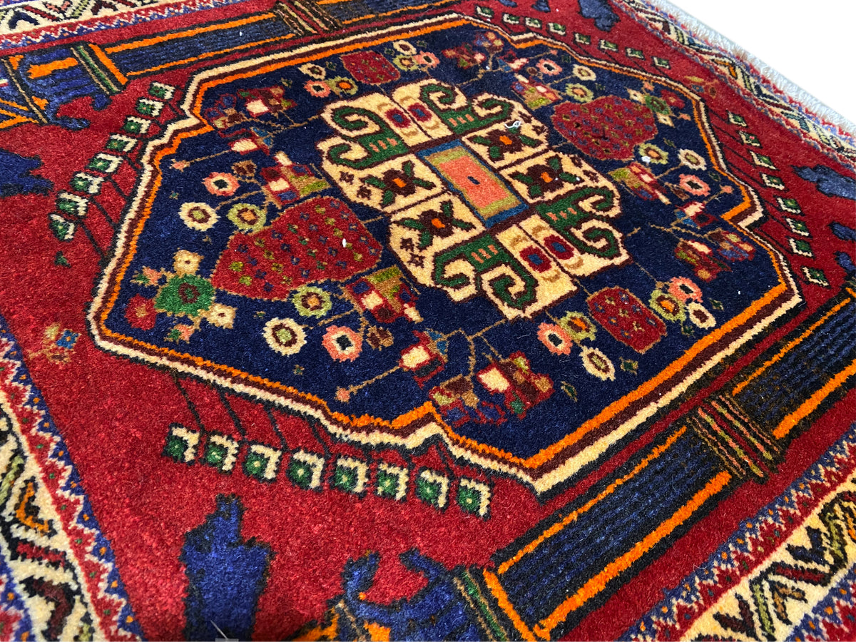 Alfombra Poshti 66x62 cm Detalle: motivo central rojo, campo azul y líneas decorativas multicolores.