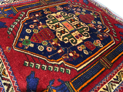 Alfombra Poshti 66x62 cm Detalle: motivo central rojo, campo azul y líneas decorativas multicolores.