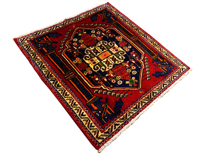 Alfombra Poshti de 66x62 cm extendida: campo interior rojo con diseño geométrico y motivos en las esquinas.