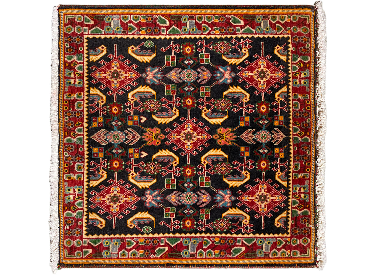 Alfombra con un patrón ornamental cuadrado, negro como base, con tonos rojos, amarillos y verdes