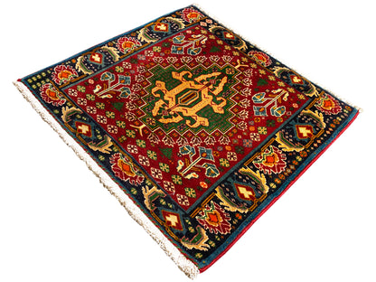 Alfombra rectangular (67x66 cm) con centro rojo, borde oscuro y ornamentos multicolores, flecos