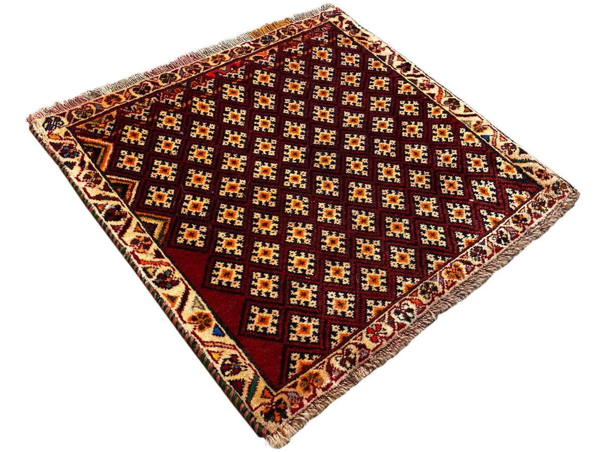 Alfombra Poshti de 61x59 cm: cuadrada, fotografiada en diagonal, con un patrón geométrico y flecos en las esquinas