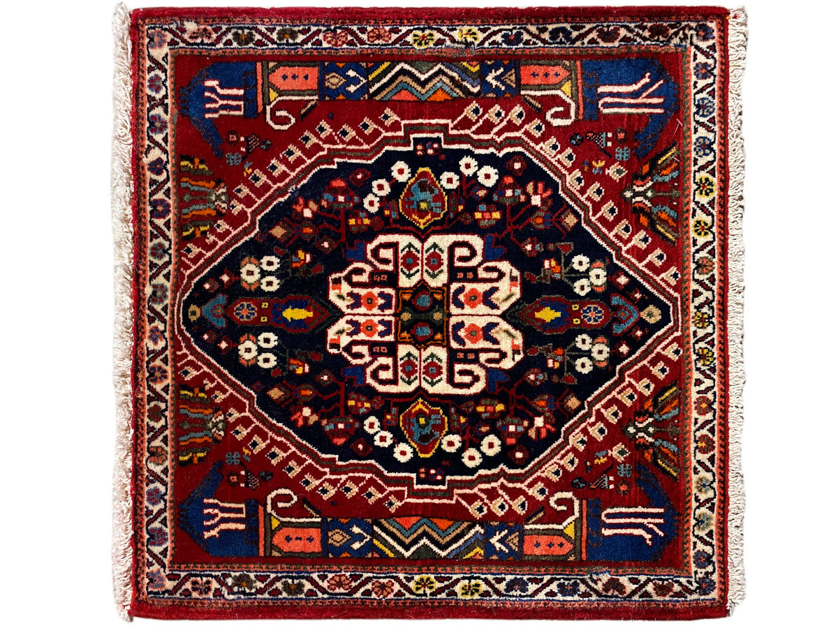 Alfombra rectangular con borde rojo, campo interior azul oscuro y patrón geométrico