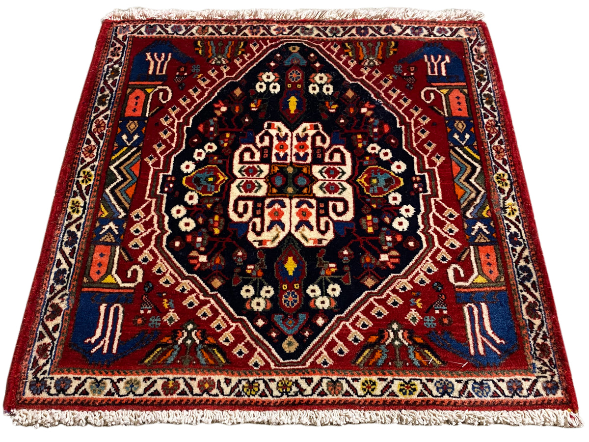 Alfombra con borde rojo, centro azul oscuro y adornos multicolores, flecos