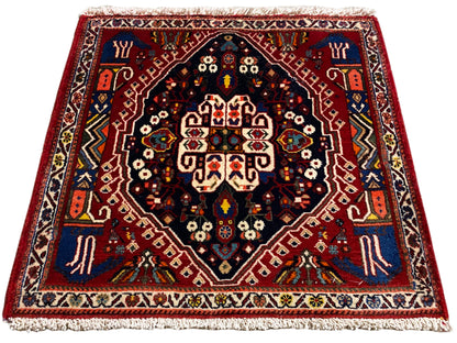Alfombra con borde rojo, centro azul oscuro y adornos multicolores, flecos
