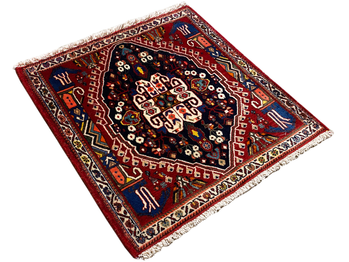 Alfombra de aspecto cuadrado con fondo rojo, medallón central azul oscuro y flecos