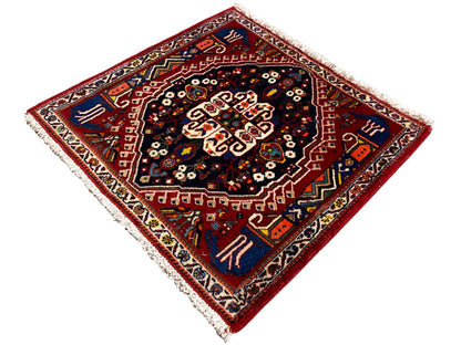 Alfombra con borde rojo y centro azul oscuro, adorno en forma de estrella, flecos