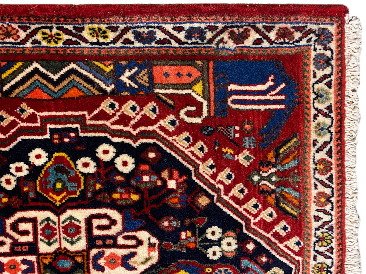 Vista detallada de la alfombra: fondo rojo, campo azul oscuro, ornamentos y cenefa