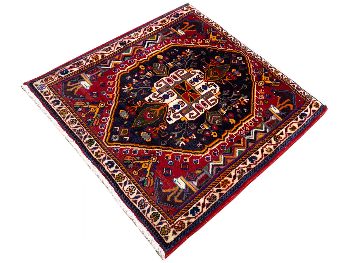 Alfombra de 70x67 cm: motivo ornamental oscuro en el centro, paleta de colores rojos y azules, cenefa en el borde