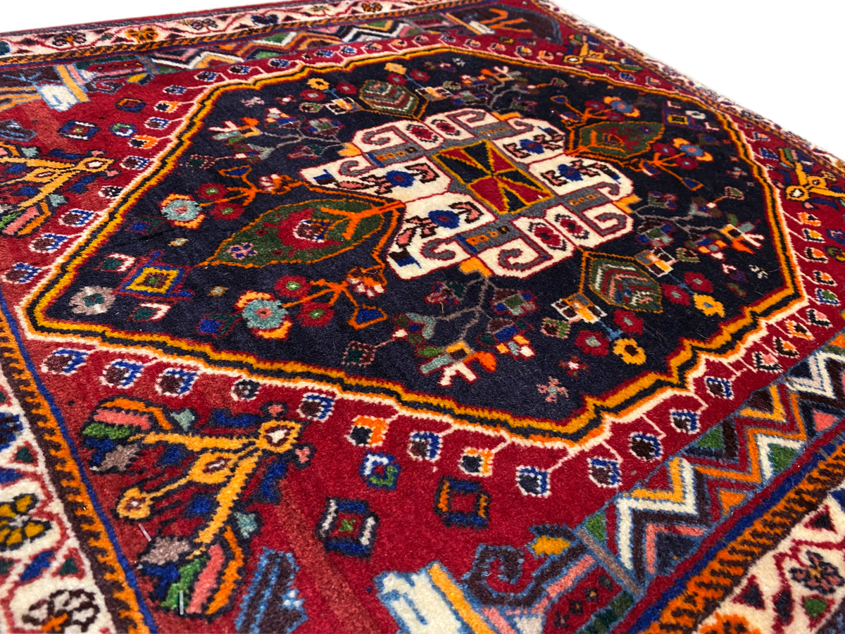 Primer plano de la superficie de una alfombra con un ornamento geométrico en azul, rojo y dorado