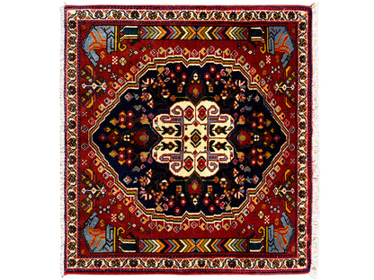 Alfombra Poshti de 65x61 cm con borde rojo, motivo central oscuro y ornamentos coloridos