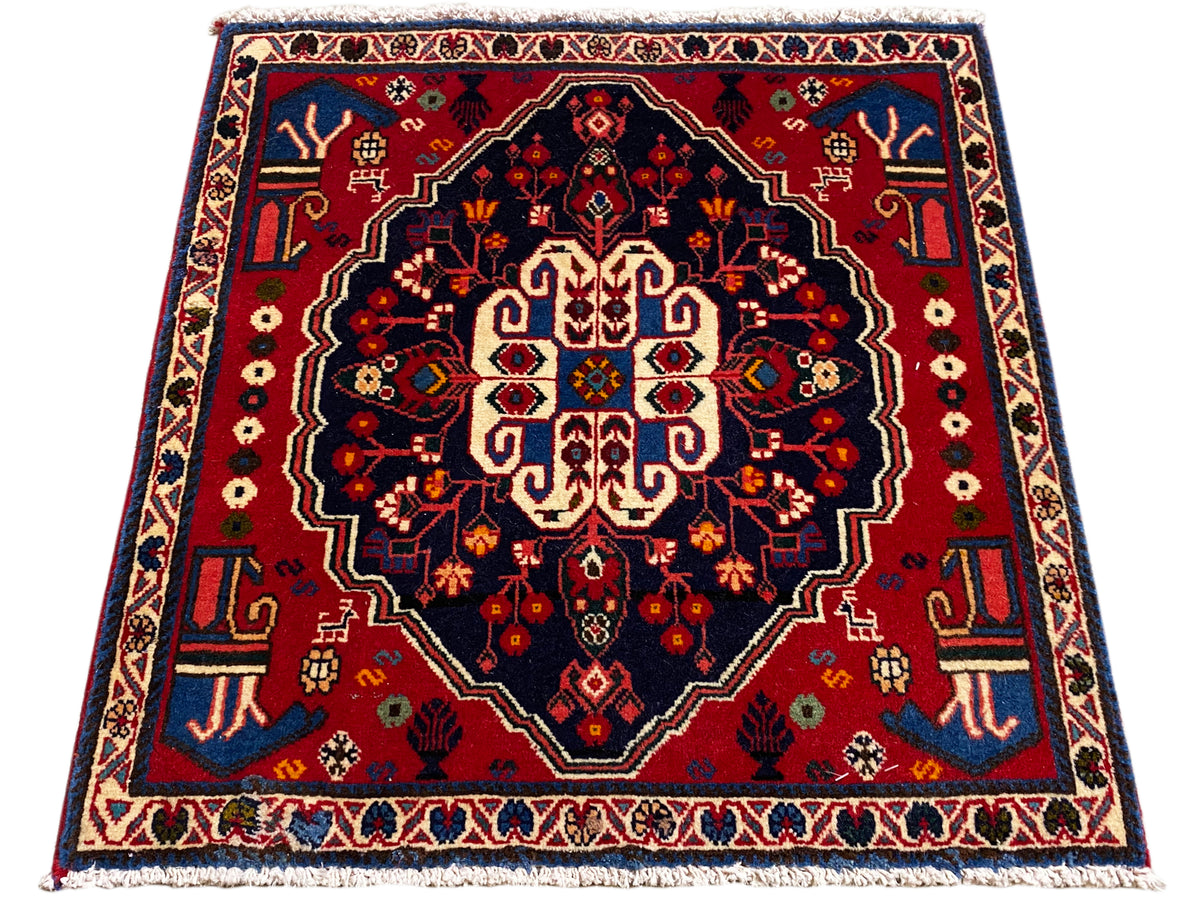 Alfombra cuadrada con borde rojo y campo oscuro, ornamento central estilizado