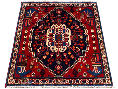 Alfombra cuadrada con borde rojo y campo oscuro, ornamento central estilizado