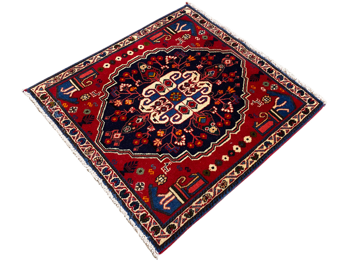 Alfombra cuadrada con centro rojo, borde azul y una fina cenefa ornamental